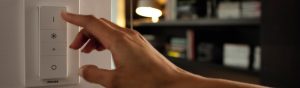 "Hand adjusting Philips smart LED dimmer switch, controlling ambient lighting in cosy living room with bookshelves."