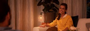 "Cosy living room ambiance created by warm LED table lamp, illuminating woman in yellow sweater enjoying evening conversation."
