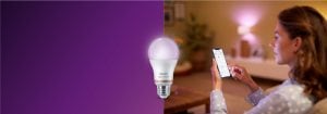 "Woman controlling smart LED lighting via smartphone app, creating warm ambiance in cosy living room with connected home technology."