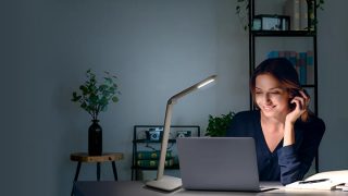 Woman studying at desk with adjustable LED task lamp, providing optimal illumination for homework in colorful home learning space.